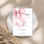 11th birthday Invitation card with a pink bow on a white background, placed on a round surface with dried plants.