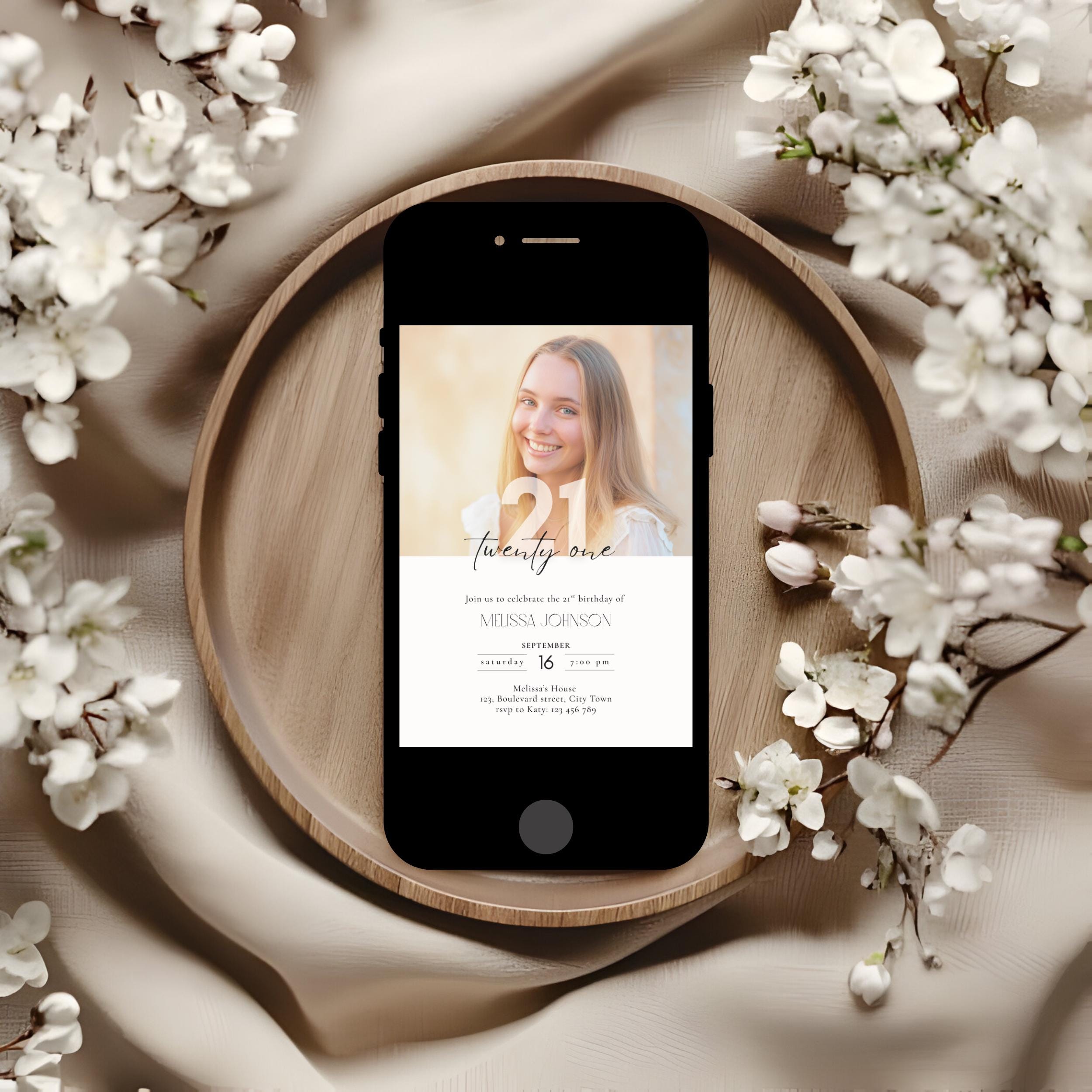 Phone displaying a wedding invitation on a wooden plate with white flowers