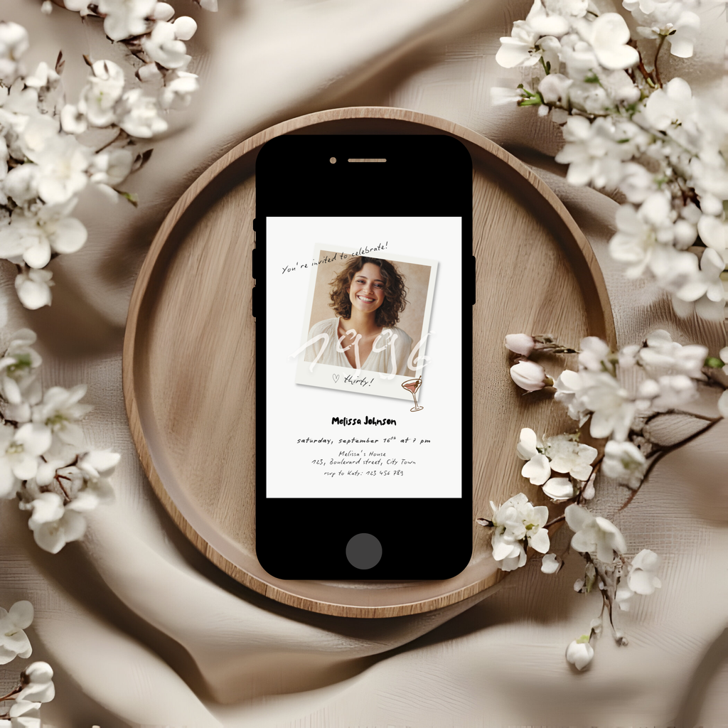 Phone with a 30th birthday invitation on a wooden plate surrounded by white flowers