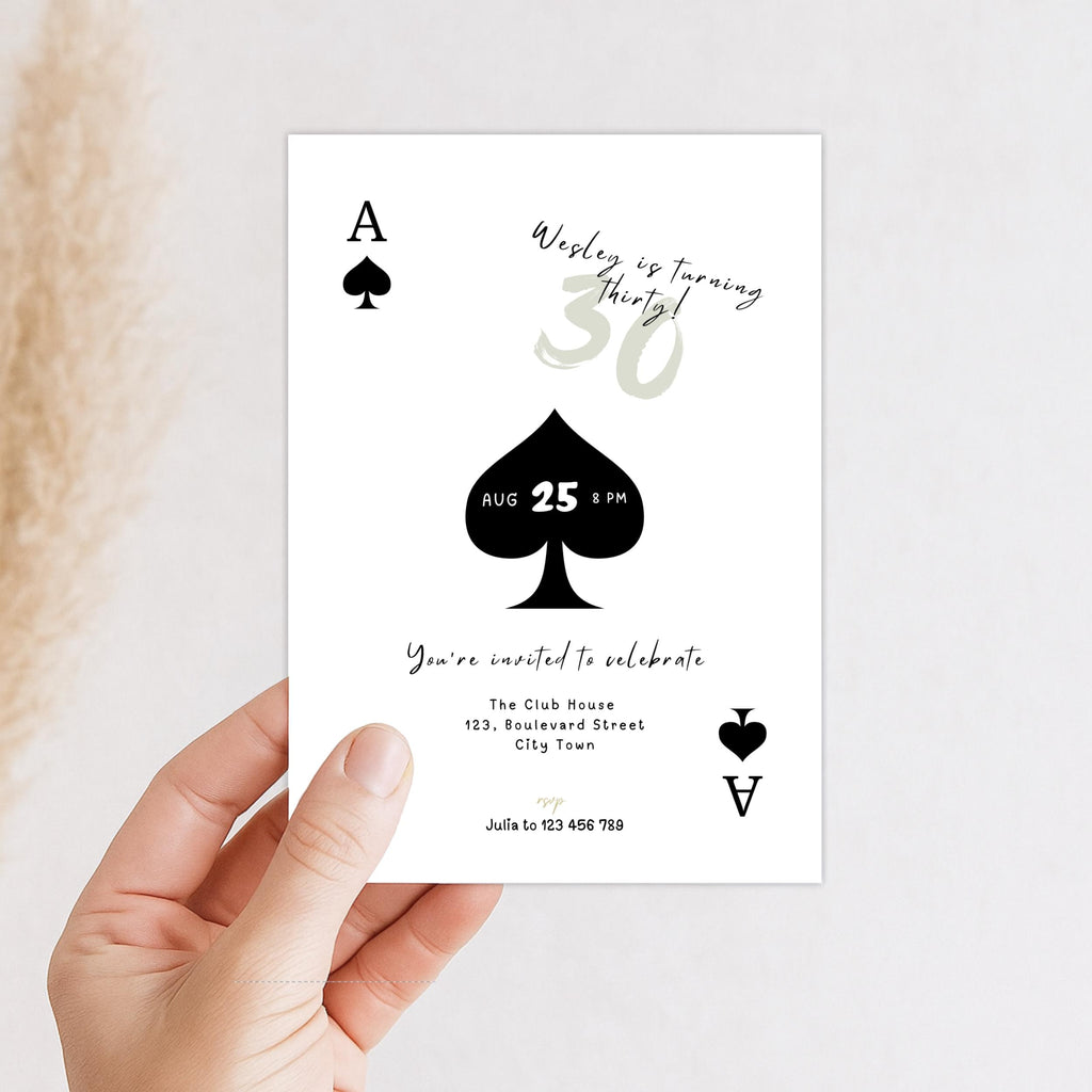 Hand holding a playing card-themed birthday invitation with spade symbols and text.