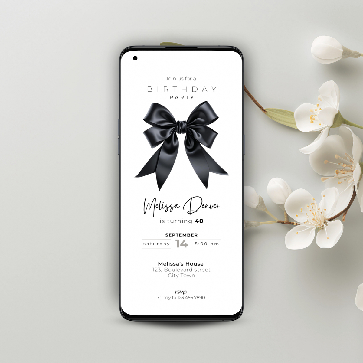 Phone displaying a black bow 40th birthday party invitation with a black bow on a light gray background with flowers.