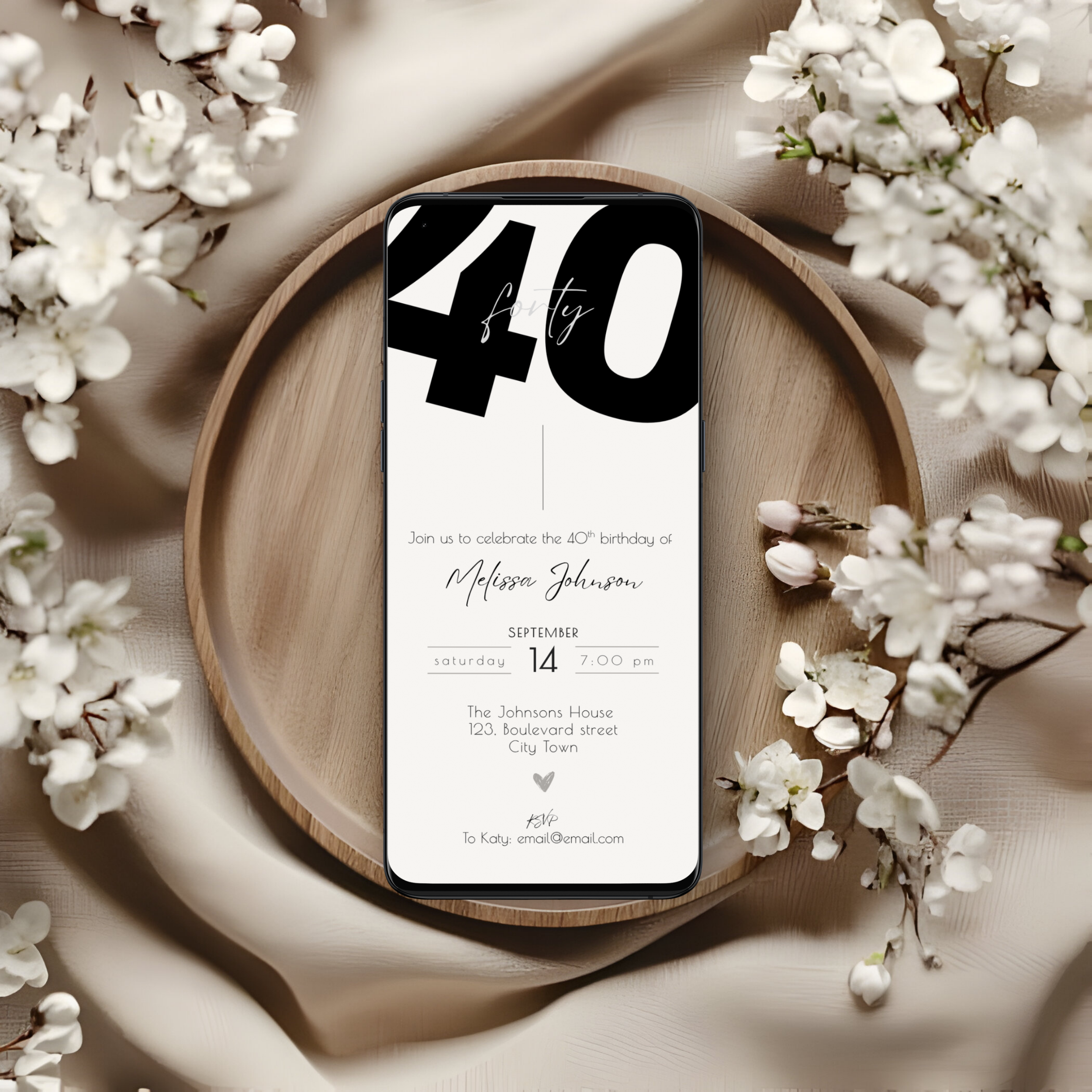 Phone displaying a 40th birthday invitation on a wooden plate with white flowers