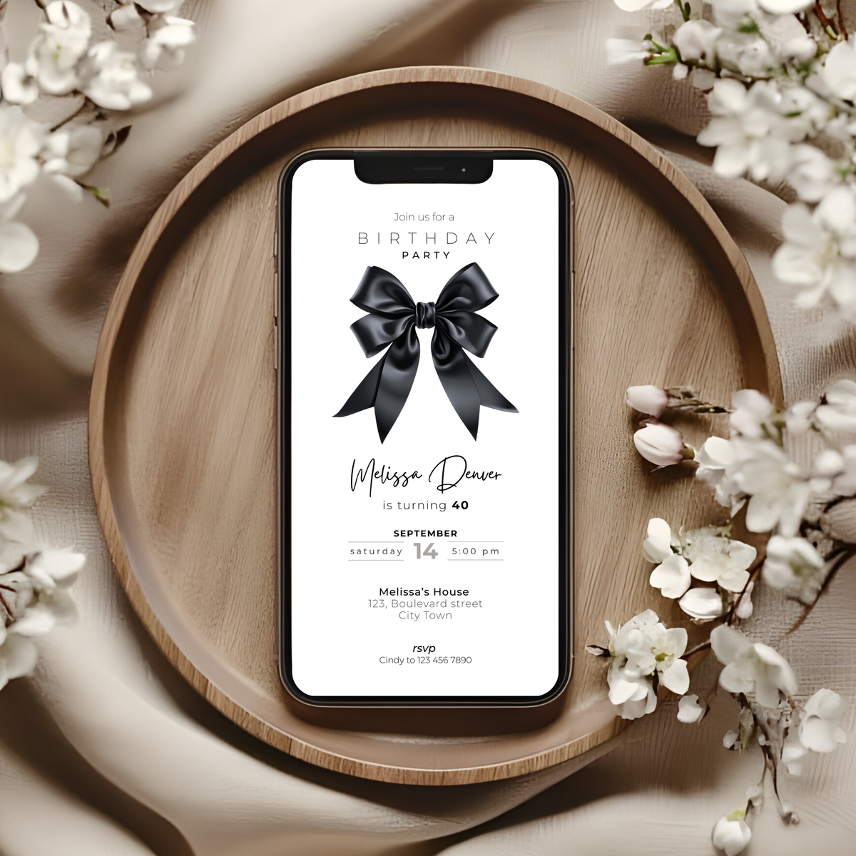 Phone displaying a black bow 40th birthday party invitation with a black bow on a light gray background with flowers.