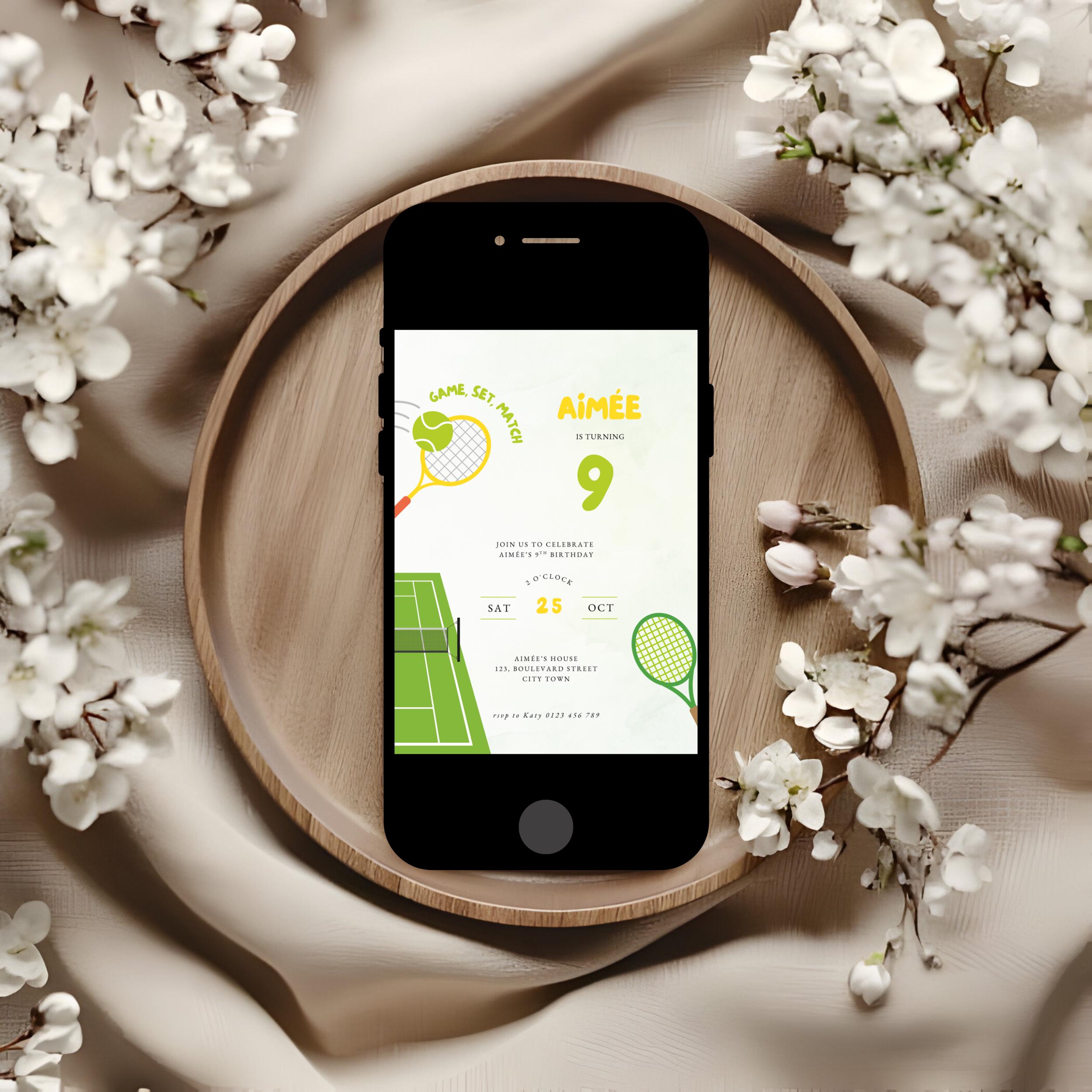Phone with a tennis-themed 9th birthday invitation on a wooden plate surrounded by white flowers