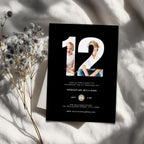 Black 12th birthday invitation card with photos of a woman and child, on a light surface with dried flowers.