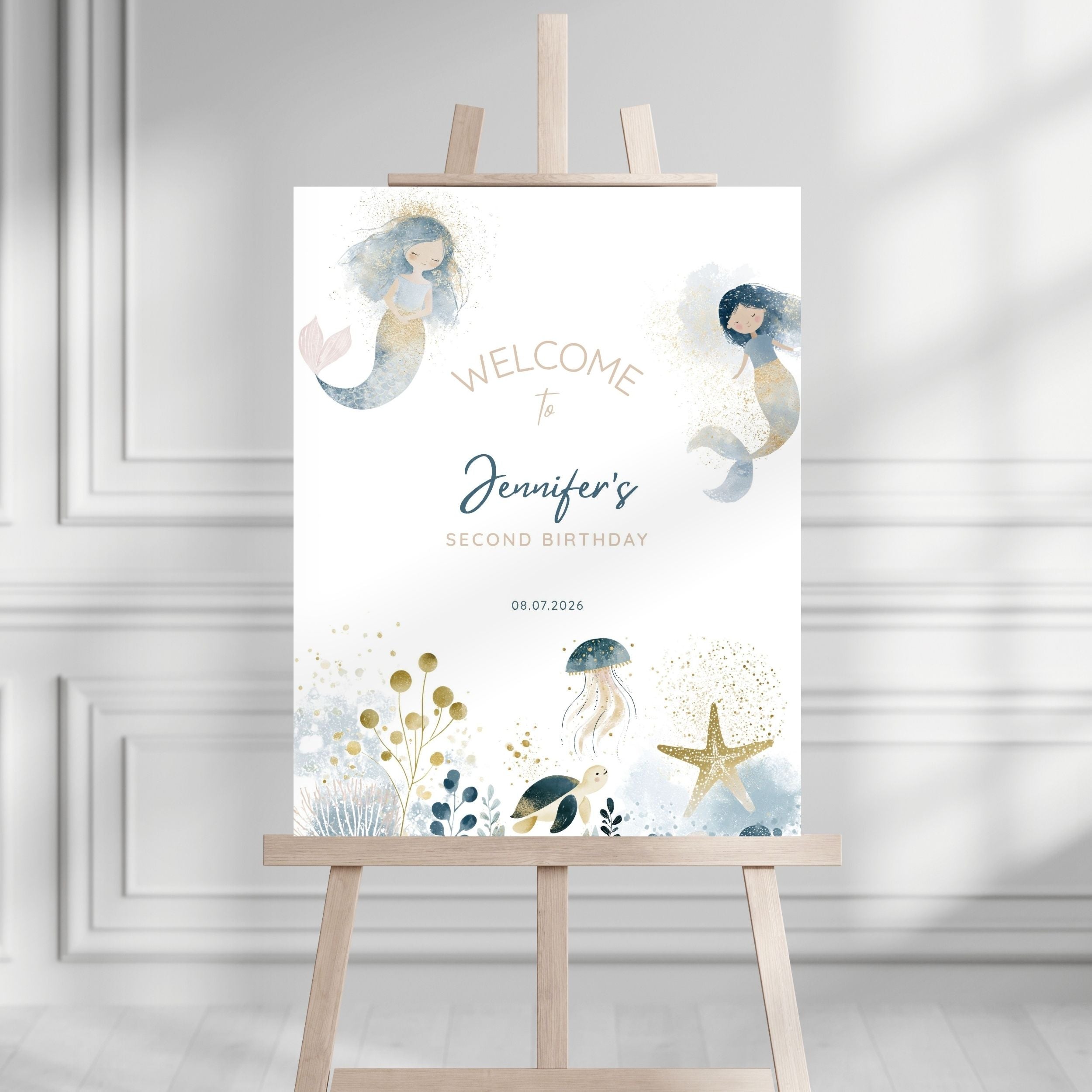 A personalized mermaid-themed second birthday welcome sign displayed on a wooden easel in a bright, modern room with white paneled walls. The sign features watercolor illustrations of two mermaids, a jellyfish, a starfish, and sea plants in soft blue, gold, and gray tones, with customizable text reading 'Welcome to Jennifer's Second Birthday' and the date '08.