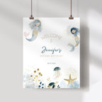 A hanging personalized baby shower sign with a white background, featuring watercolor mermaids, jellyfish, a starfish, and gold glitter-style accents. The text reads 'WELCOME to Jennifer's SECOND BIRTHDAY' with the date '08.