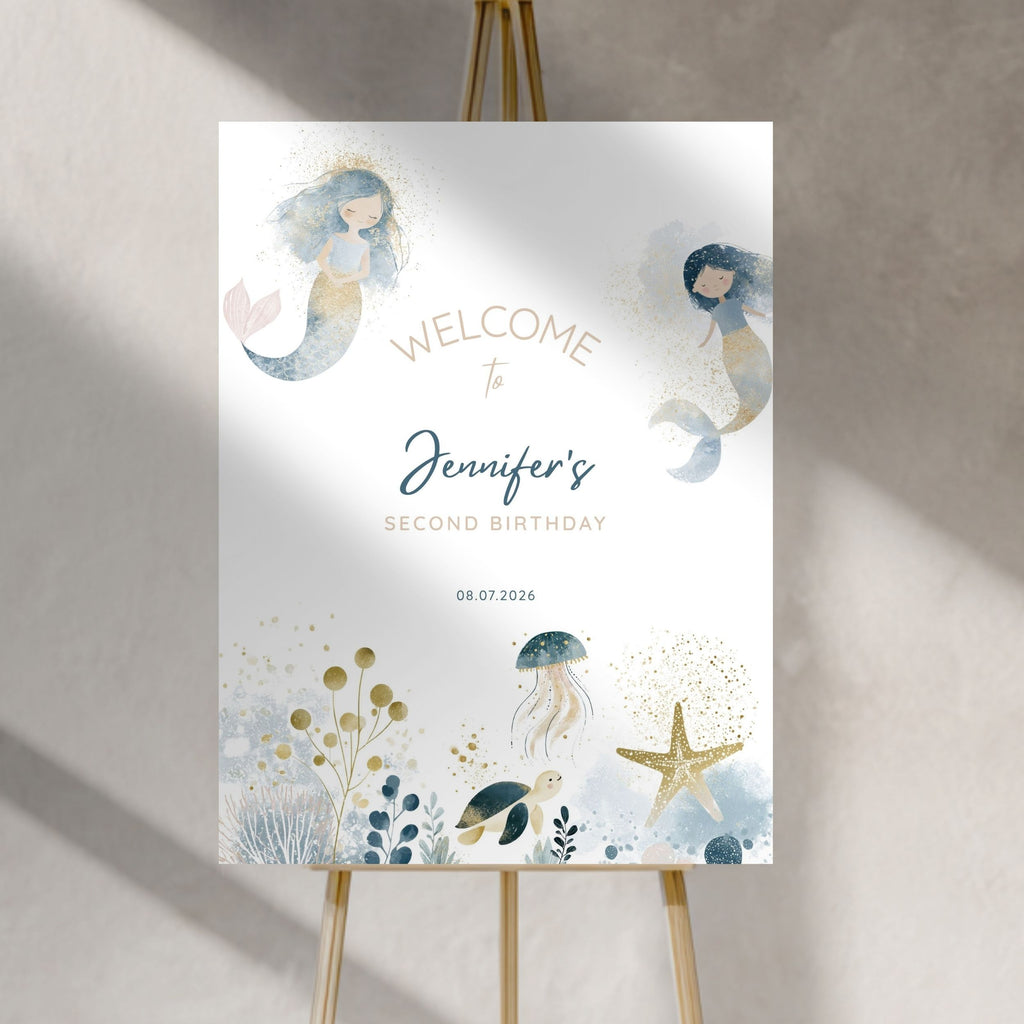 A vertical welcome sign for a second birthday party, displayed on a wooden easel against a textured light gray wall. The sign features watercolor illustrations of mermaids, a jellyfish, a turtle, a starfish, and gold glitter accents on a white background, with the text 'WELCOME to Jennifer's SECOND BIRTHDAY' and the date '08.