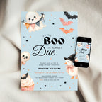A Halloween baby shower invitation card with cute ghost, bat, and cupcake illustrations on a light blue background, styled on a cream fabric surface next to a smartphone showing the digital version of the invitation.