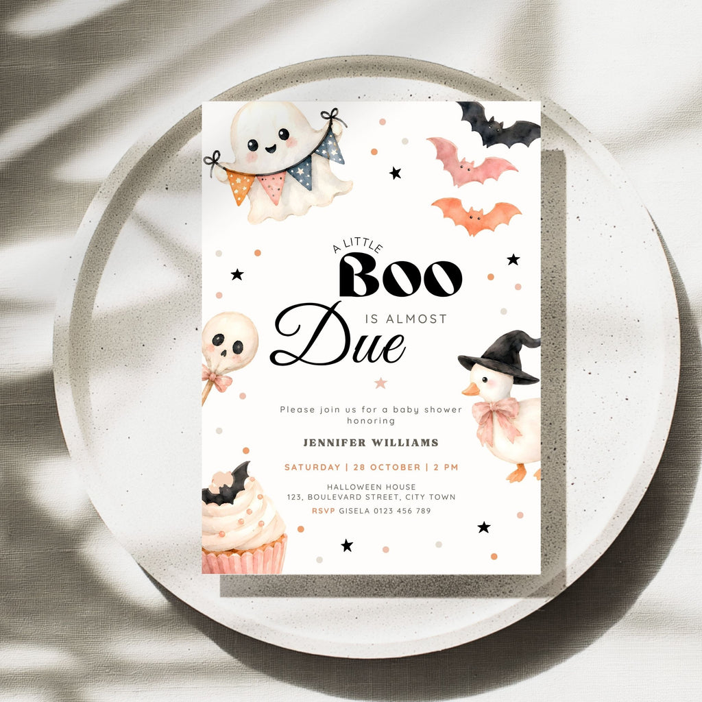 A Halloween baby shower invitation card styled on a round white tray with soft leaf shadows. The invitation features cute watercolor illustrations of a ghost, bats, a pumpkin, a cupcake, and a witch hat around the text 'A Little Boo Is Almost Due'.