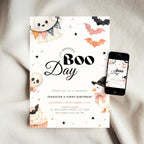 A Halloween-themed first birthday invitation card is styled on a soft beige fabric background next to a smartphone showing the matching digital design. The card features cute watercolor illustrations of a ghost, bat, skull, cupcake, and a witch, with the text 'It's Jennifer's Boo Day'.