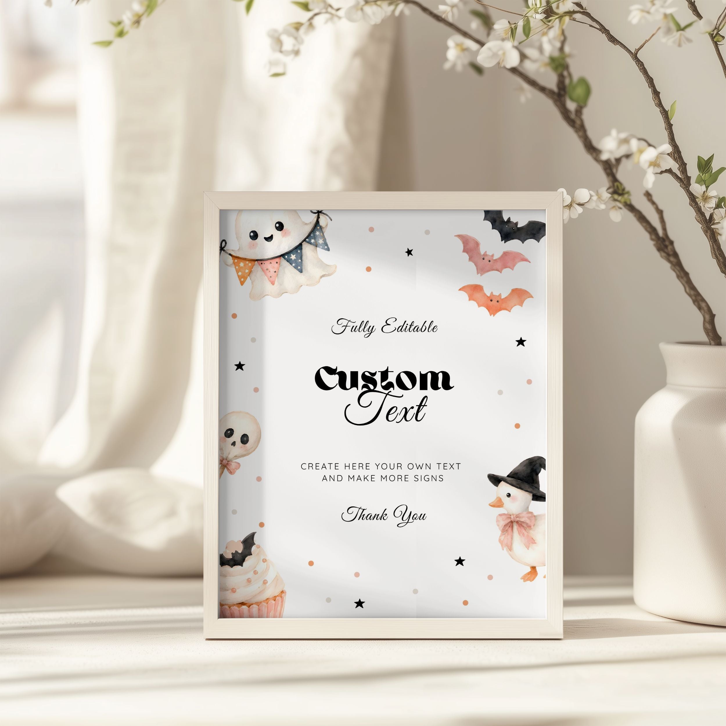 A framed customizable Halloween sign with cute watercolor illustrations of a ghost, cupcake, snowman, bat, and stars, styled on a tabletop next to a white vase with blossoms.