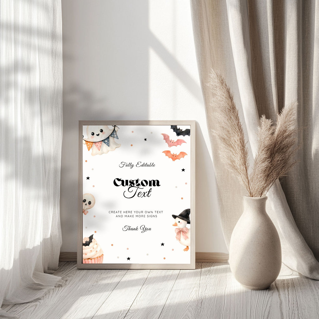 A framed custom Halloween greeting card with cute watercolor illustrations of a ghost, cupcakes, bats, and a witch, styled in a bright room next to a vase of pampas grass.