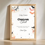 A framed editable sign template with a light wood frame, featuring Halloween illustrations like a ghost, bat, cupcake, and snowman, plus customizable text on a white background.