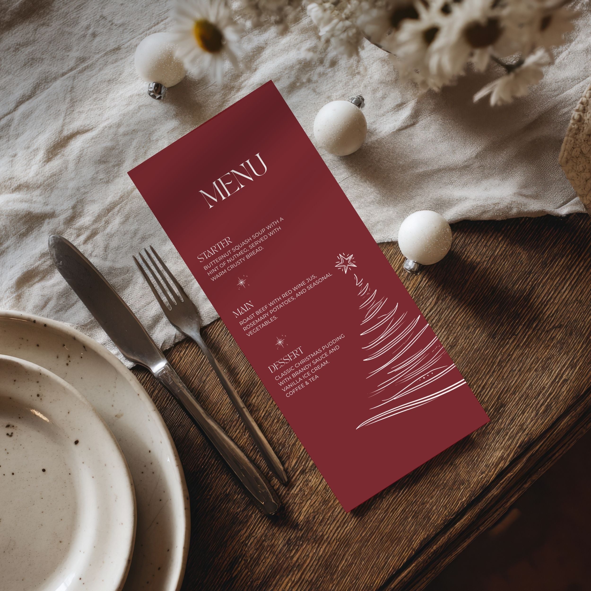 A burgundy Christmas-themed menu card with white text and a tree illustration, styled on a wooden table with a plate, fork, knife, and white decorative ornaments.