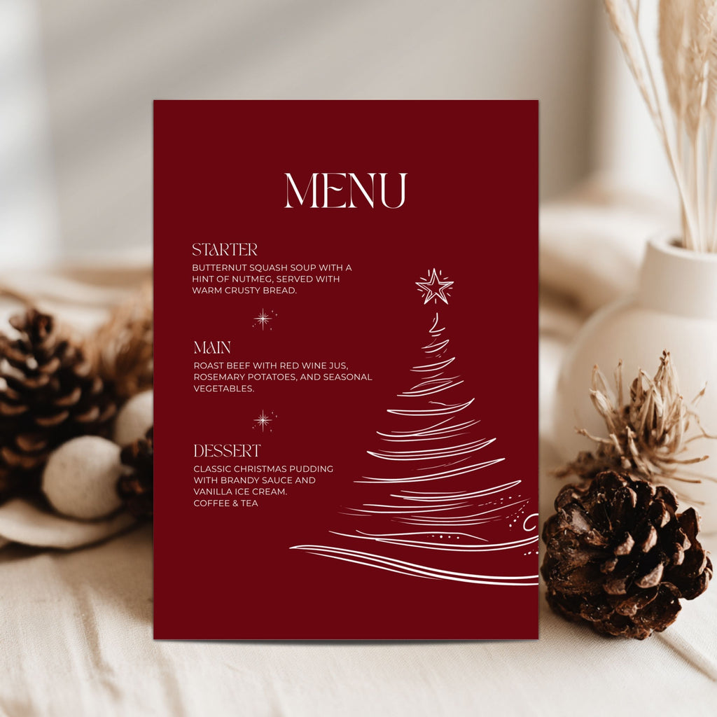 A vertical red menu card with white text reading 'MENU' and holiday dish descriptions, styled on a light surface with pinecones and dried grass in the background.