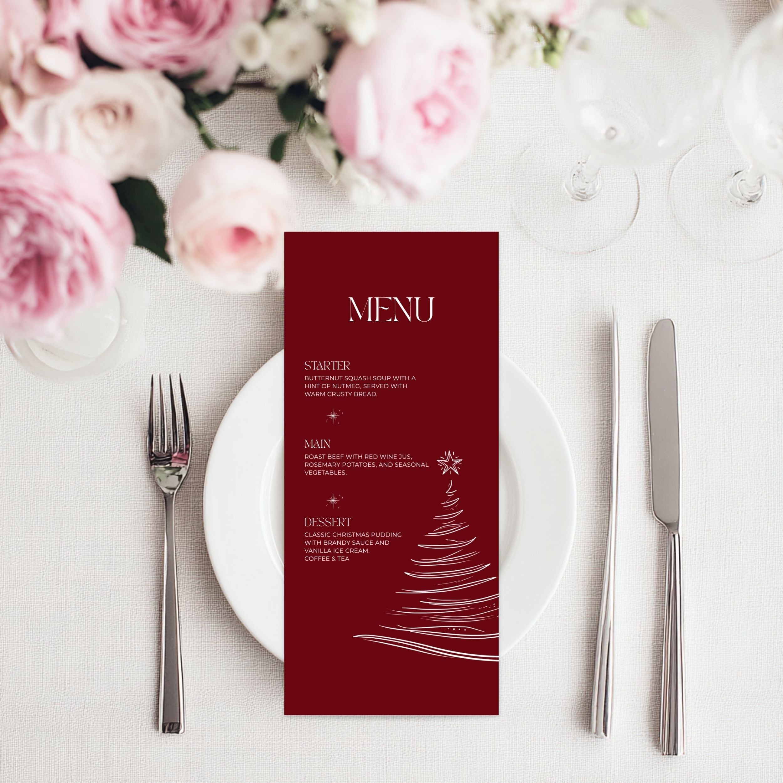 A vertical burgundy christmas menu card with white text and a white Christmas tree illustration, styled on a white plate with silver cutlery and pink flowers in the background.