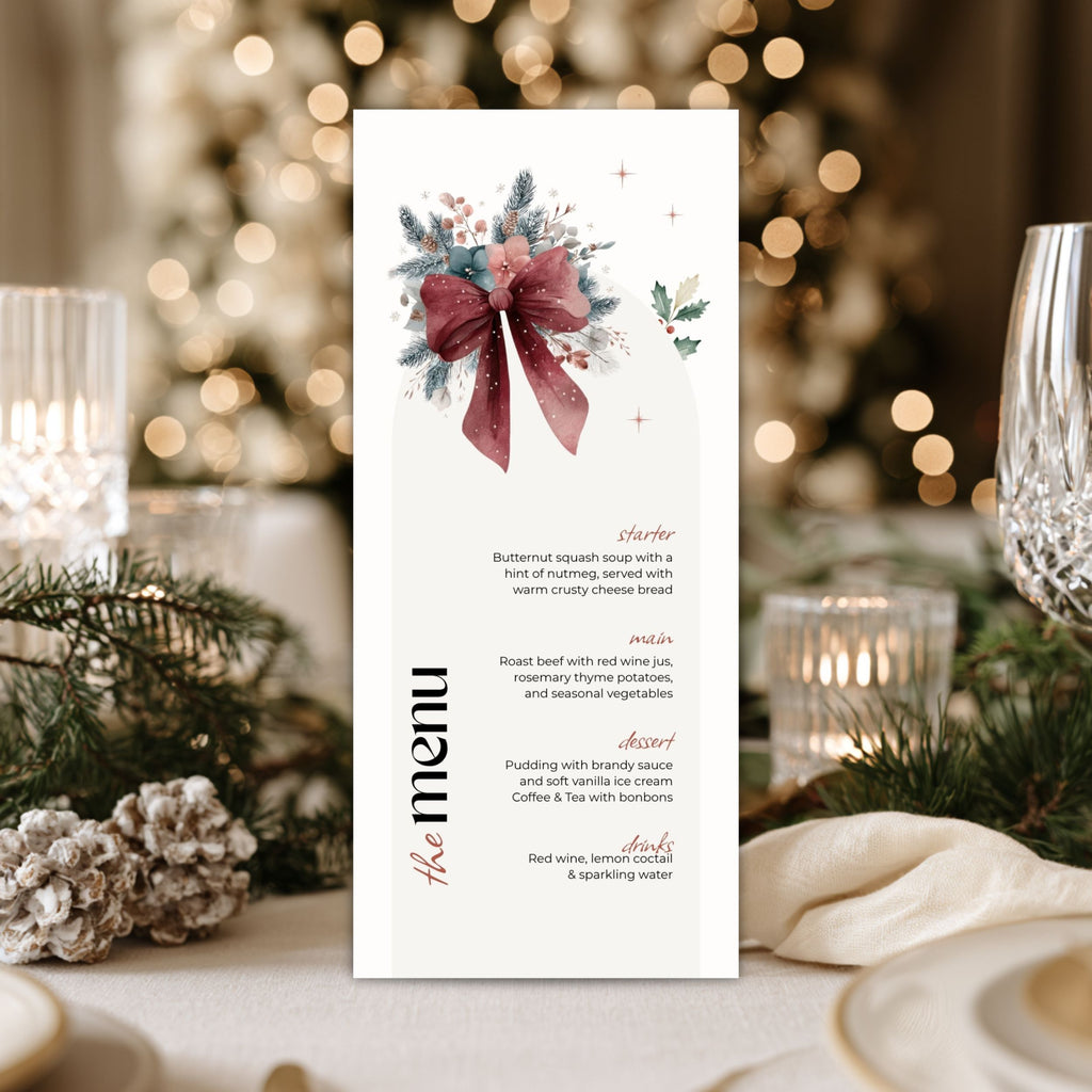 A vertical chrsistmas menu card with a watercolor floral and bow illustration at the top, styled on a table with candles, plates, pine branches, and a blurred Christmas tree in the background.
