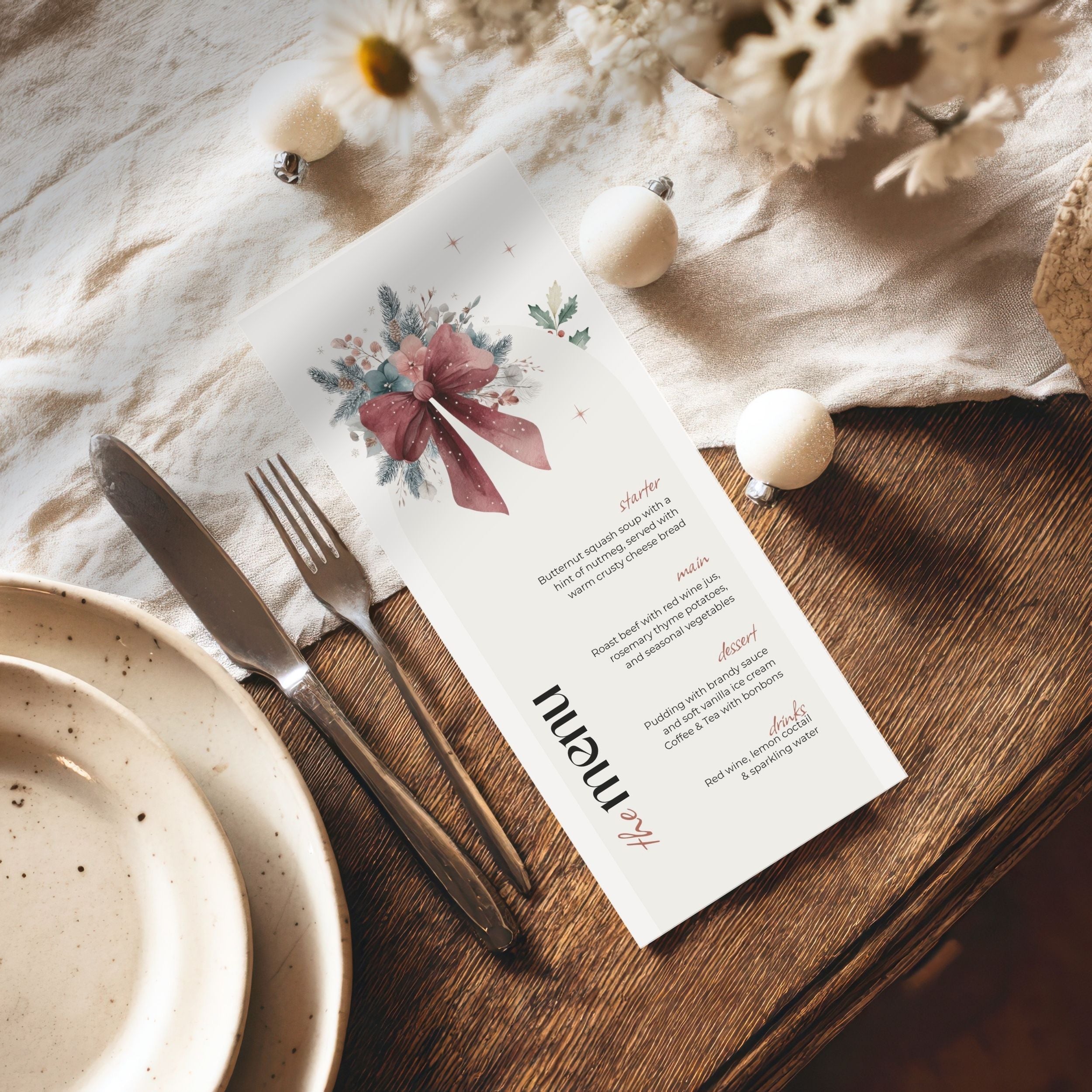 A printed christmas or event menu card laid on a wooden table with a knife, fork, plates, and dried flowers around it. The card is white with a floral bow illustration and small decorative text.
