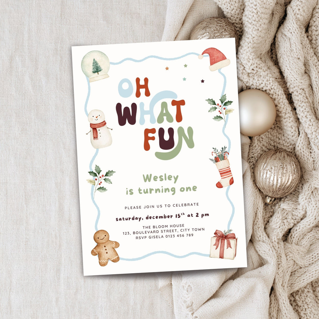 A festive Christmas-themed birthday invitation card for Wesley, styled on a light wood surface next to a cozy beige knit sweater and gold ornaments.