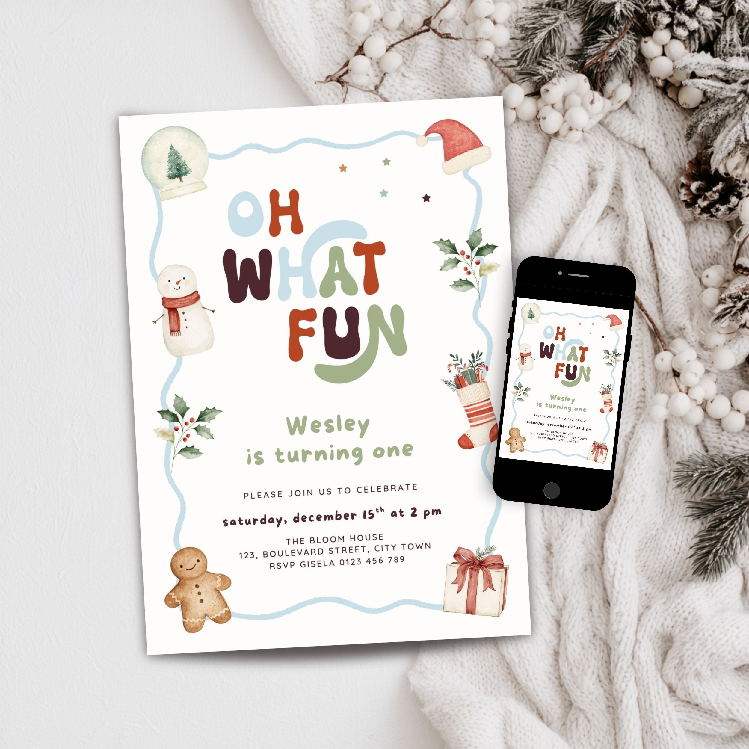 A festive Christmas-themed birthday invitation card for Wesley's first birthday, styled in a flat lay next to a smartphone displaying the digital version of the design. The card features colorful text reading 'OH WHAT FUN', a light blue border, illustrations of a snowman, gingerbread man, Santa hat, and a gift, set against a cozy background of a white knit blanket and pinecones.