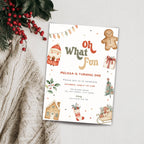 A Christmas-themed birthday invitation card styled on a light gray surface with a knitted cream sweater and red berries in the corner. The card features festive illustrations including a gingerbread man, Santa, a Christmas tree, a stocking, and the text 'Oh What Fun' and a birthday celebration invitation.