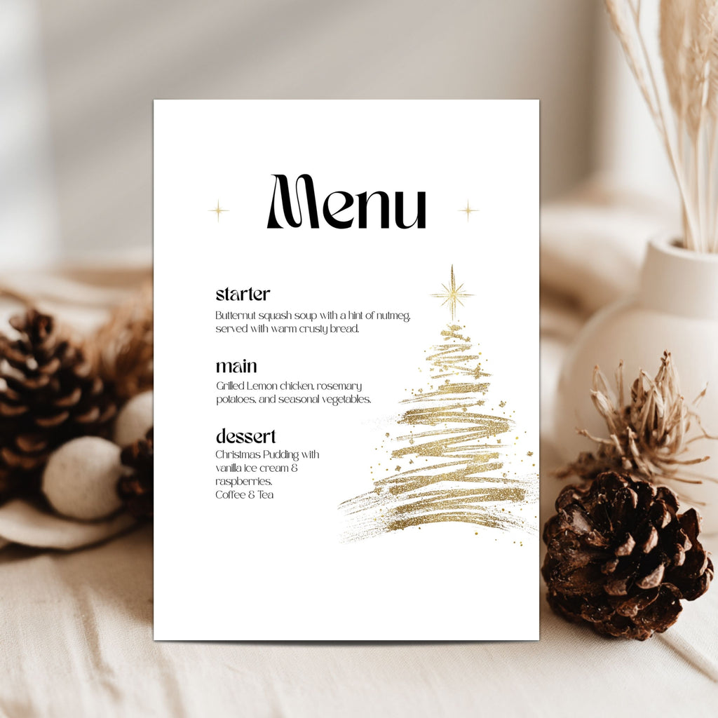 A vertical white menu card with black text and a gold glittery Christmas tree illustration, styled on a light fabric surface with pinecones and dried grass in a vase.