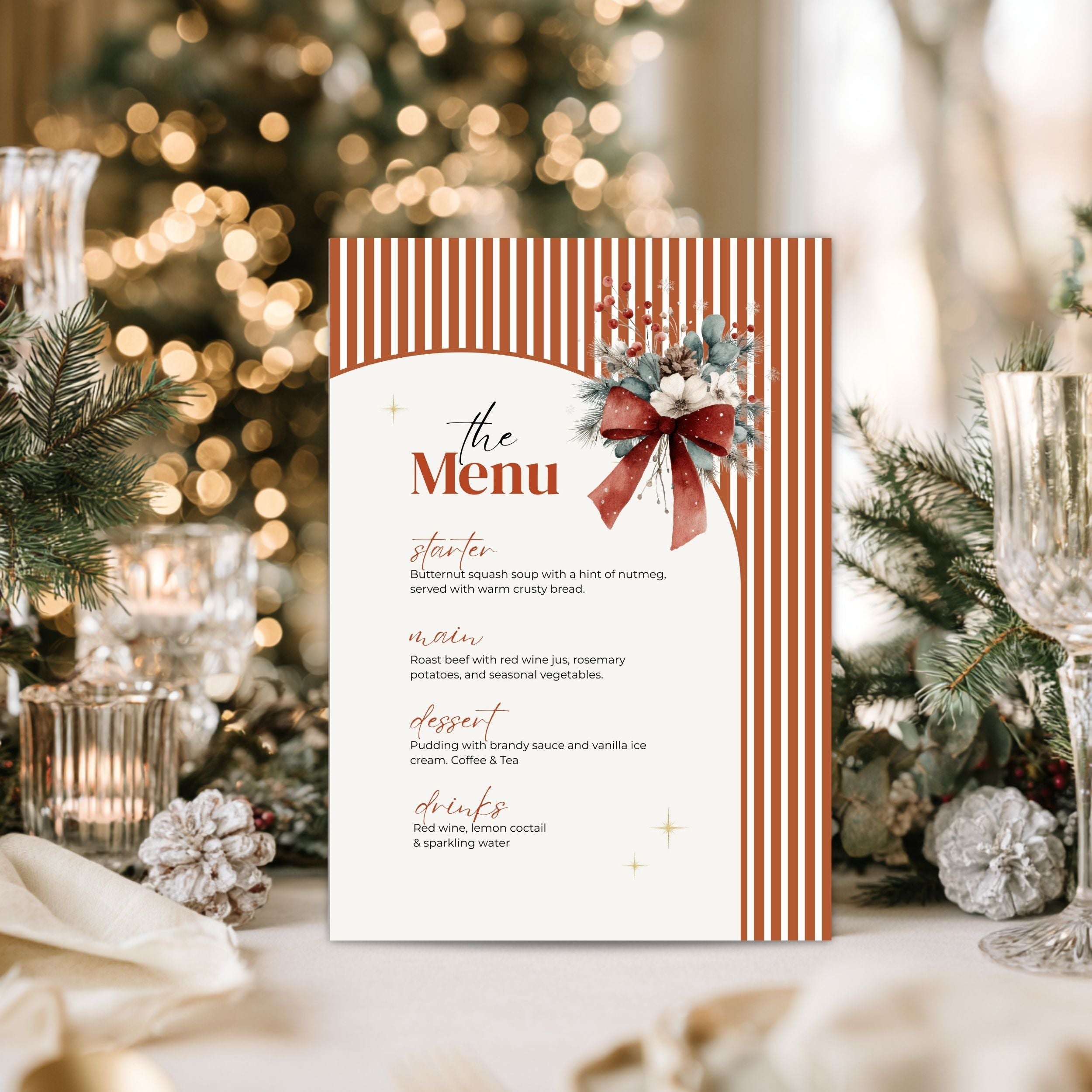 A festive holiday menu card with orange and white vertical stripes, a red bow illustration, and elegant script text, displayed on a table with blurred Christmas decorations and a tree in the background.