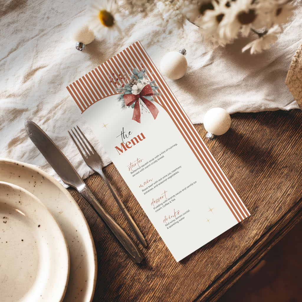 A printed paper menu card styled on a wooden table with a knife, fork, plates, and dried flowers. The menu has rust-orange striped borders, a red bow illustration, and black text reading 'The Menu' with course headings below.