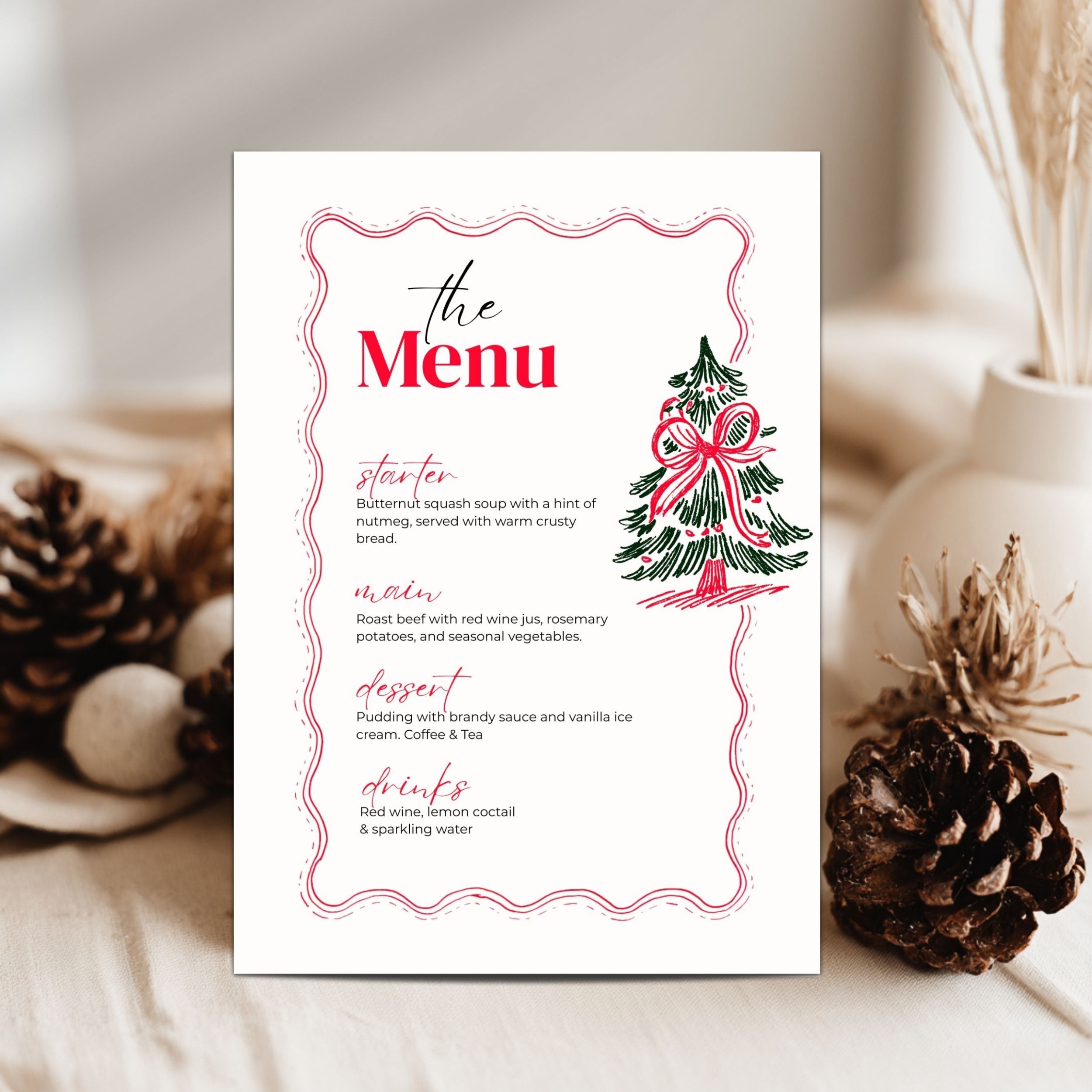 A vertical printed menu card with a white background, pink decorative border, red title text, and a small illustrated Christmas tree, styled on a tabletop with pinecones and dried stems in the background.