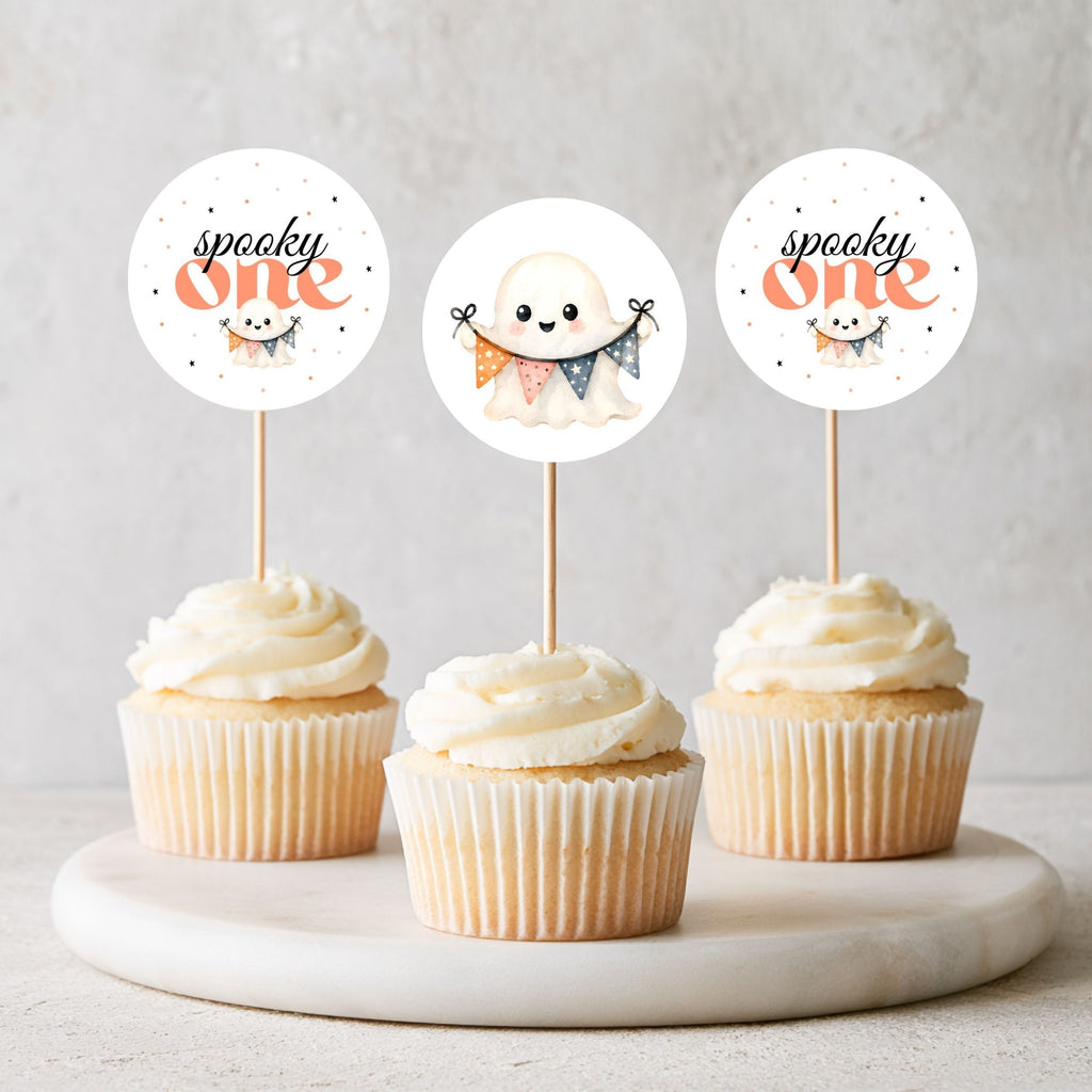 Three frosted cupcakes on a marble tray with round wooden picks featuring cute ghost illustrations and the words 'spooky one' in orange and black.