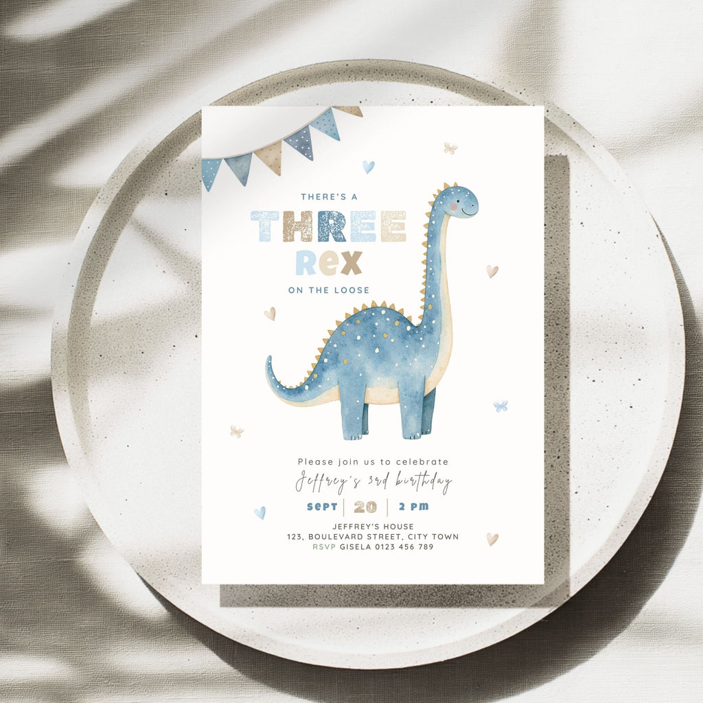 A rectangular dinosaur 3rd birthday invitation card featuring a blue long-neck dinosaur illustration, styled on top of a round speckled tray with soft shadows.