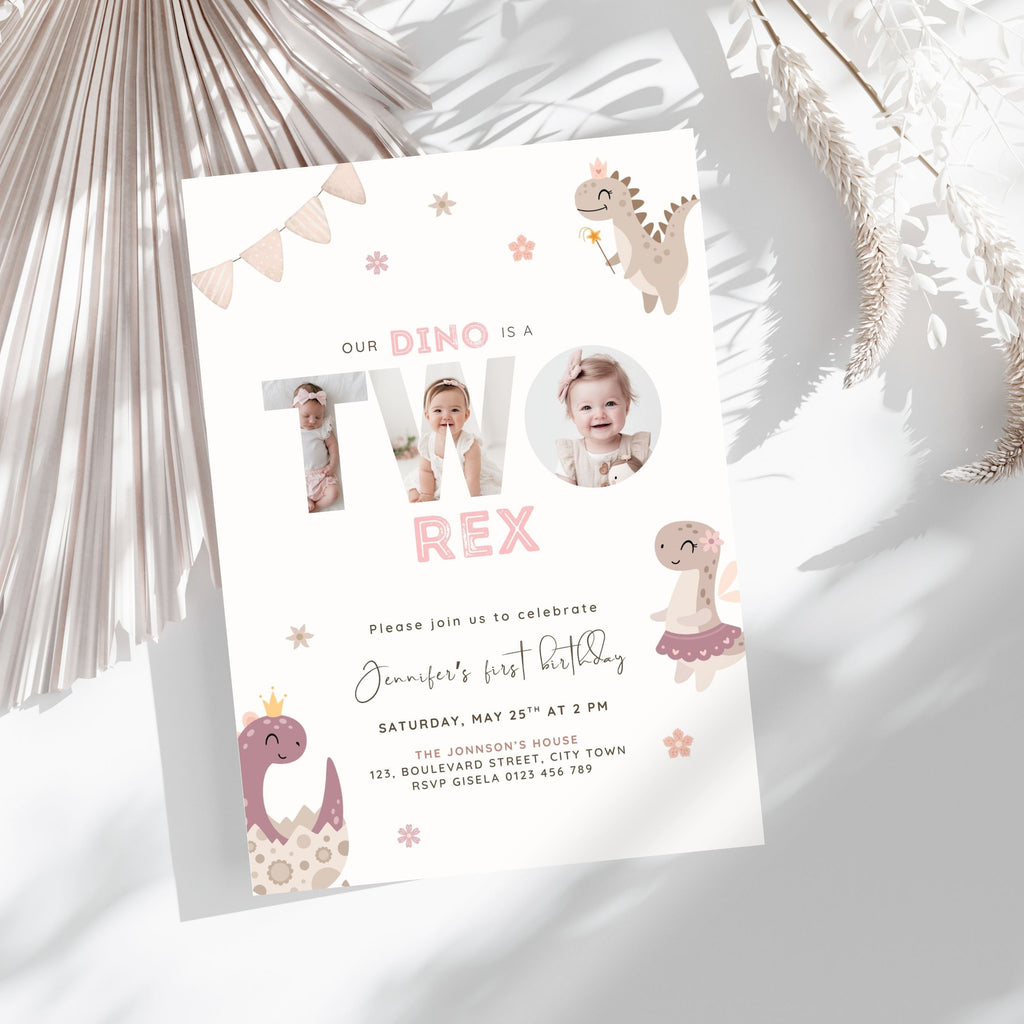 A children's dino 2nd birthday invitation card styled in a flat-lay with dried palm leaves. The card is white with pastel pink and beige dinosaur illustrations and the text 'Our Dino is a Two Rex' with two circular photo cutouts in the center.
