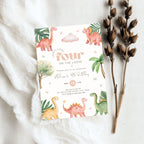 A children's 4th birthday invitation card styled in a flat lay on white fabric, accompanied by dried brown plant stems. The invitation features a whimsical dinosaur illustration design with pastel colors including pink, green, yellow, and orange on a white background.