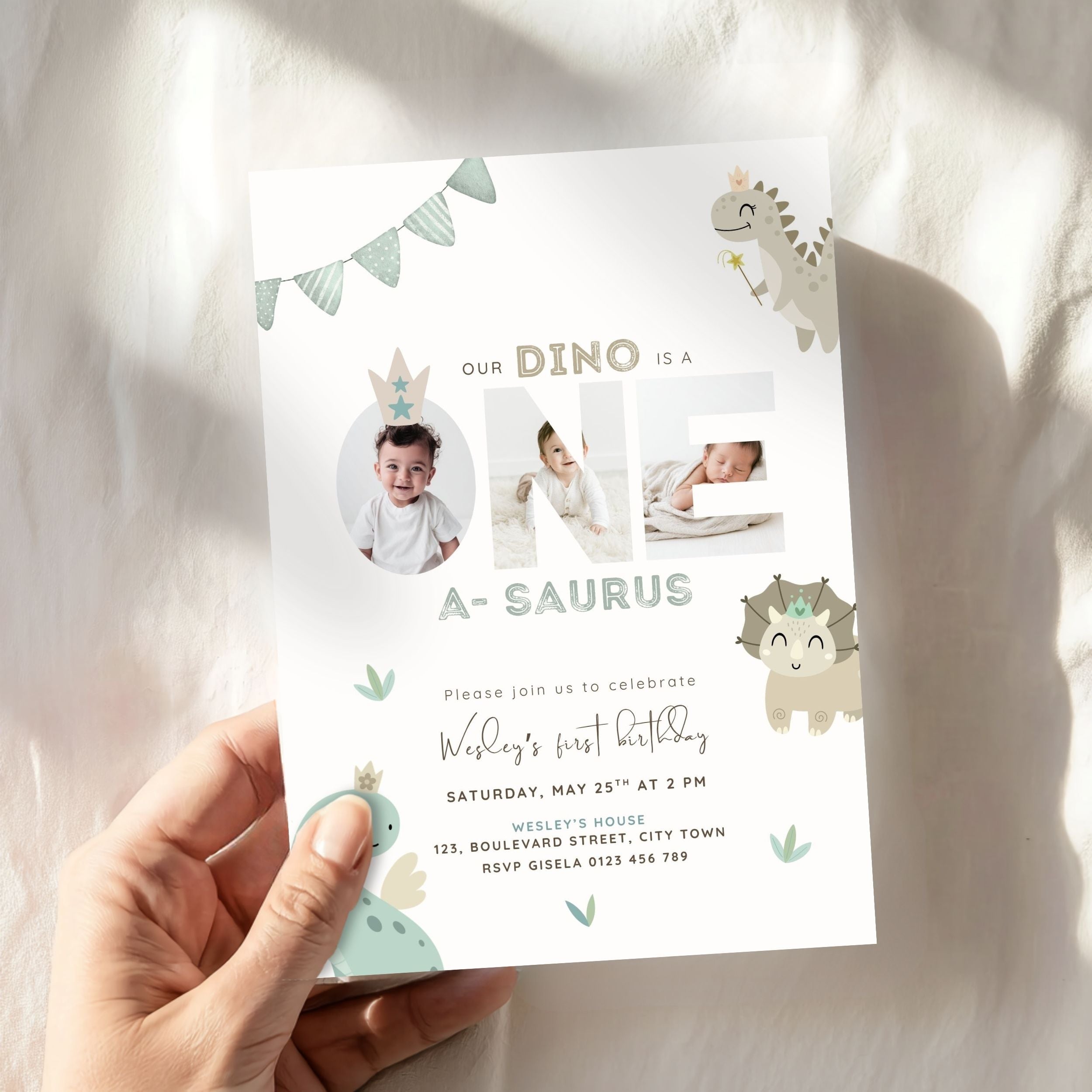 A hand holds a customizable dinosaur-themed first birthday invitation card against a soft, white draped fabric background with warm sunlight shadows.