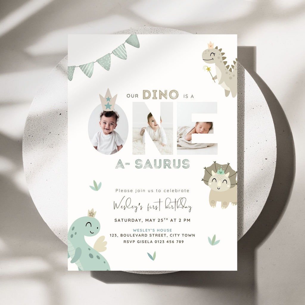 A children's first birthday invitation card with a dinosaur theme, styled flat on a round white plate with soft shadows. The card features the text 'OUR DINO IS A NE A-SAURUS' with photo placeholders, cute pastel dinosaur illustrations, and event details.