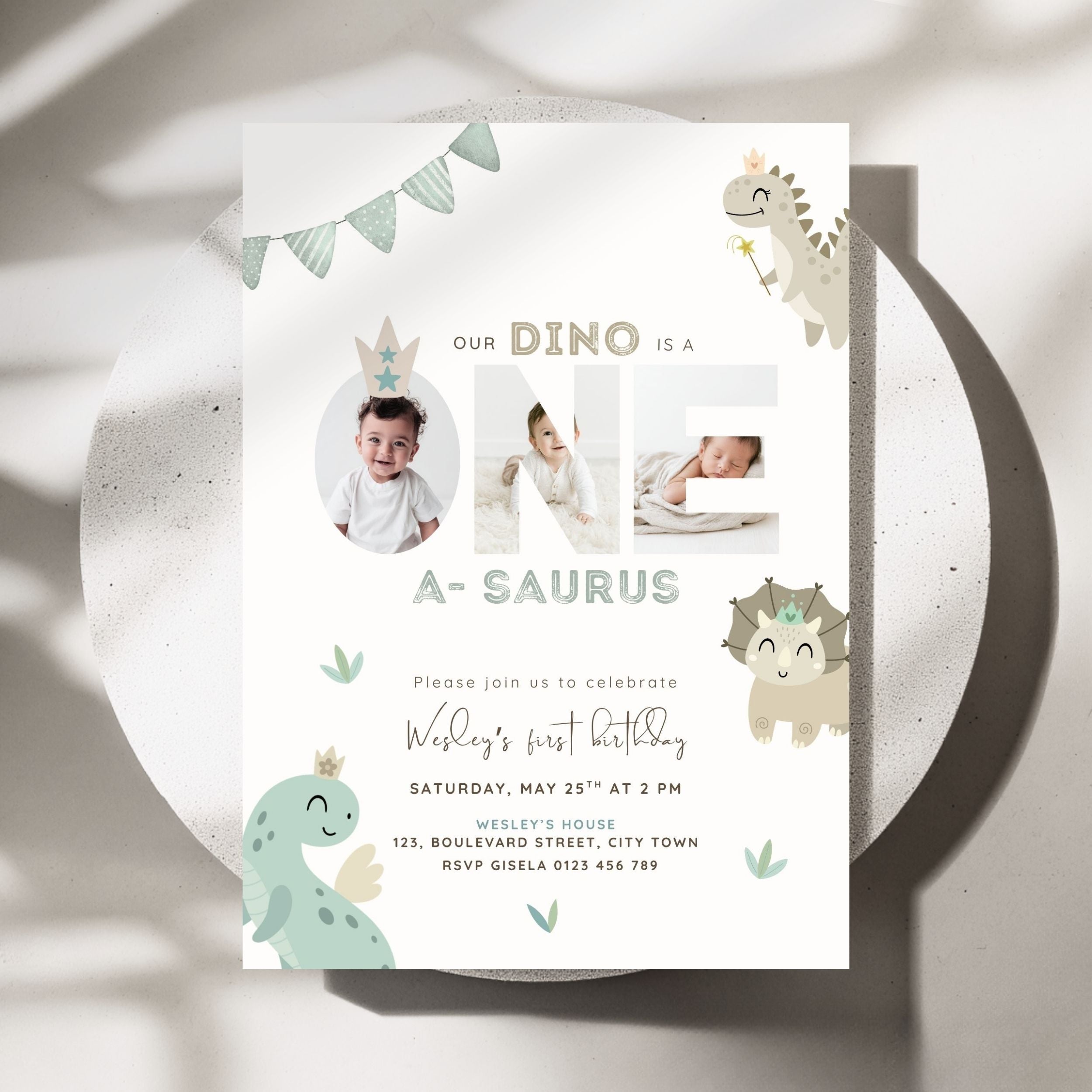 A children's first birthday invitation card with a dinosaur theme, styled flat on a round white plate with soft shadows. The card features the text 'OUR DINO IS A NE A-SAURUS' with photo placeholders, cute pastel dinosaur illustrations, and event details.