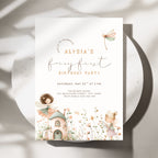 A fairy-themed birthday party invitation card displayed on a round white plate with soft shadows. The card features elegant script text reading 'Alysia's fairy first birthday party' with watercolor illustrations of a fairy, a small cottage, flowers, and a dragonfly.
