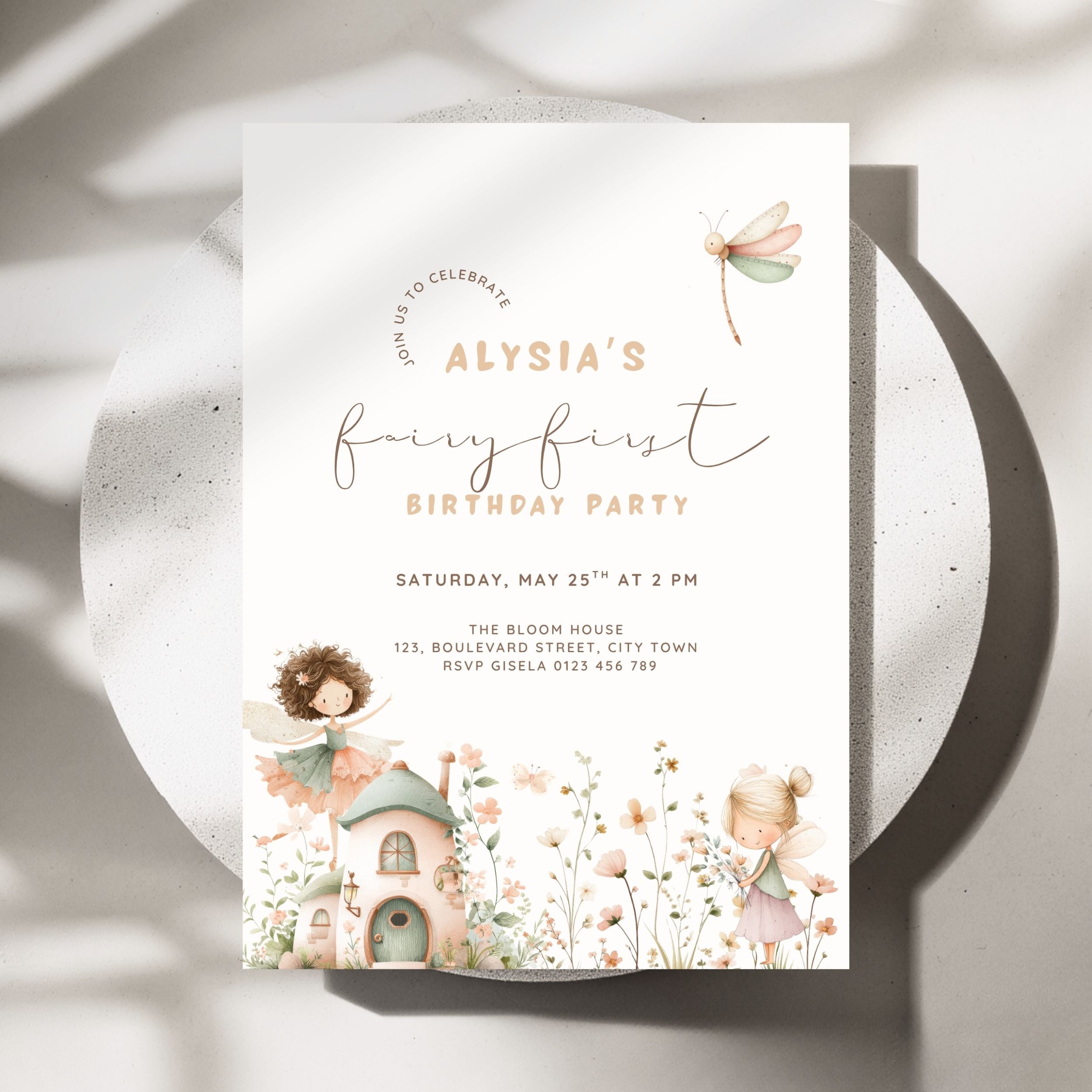 A fairy-themed birthday party invitation card displayed on a round white plate with soft shadows. The card features elegant script text reading 'Alysia's fairy first birthday party' with watercolor illustrations of a fairy, a small cottage, flowers, and a dragonfly.