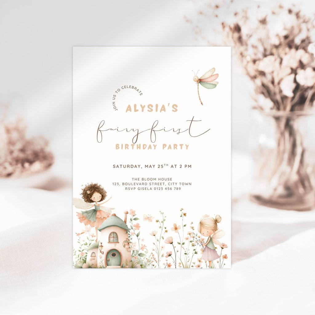 A fairy-themed first birthday invitation card featuring soft pastel illustrations of a dragonfly, a small cottage, and woodland characters on a white background, styled with dried flowers in the background.
