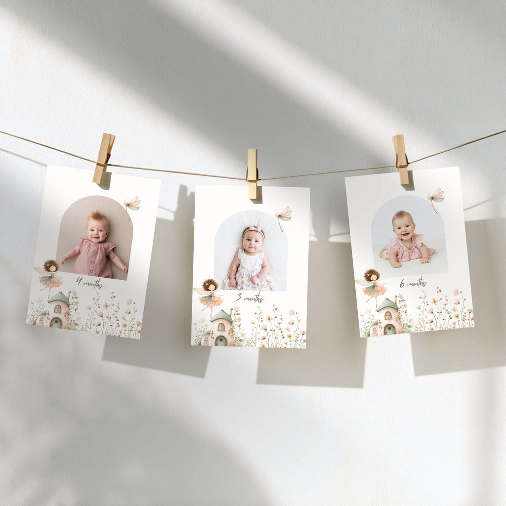 Three personalized baby milestone photos clipped to a string against a sunlit white wall, with soft shadows and delicate floral illustrations on the cards.