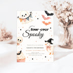 A Halloween-themed birthday invitation card displayed on a light surface with soft blurred decorative flowers in the background. The card features cute illustrations of a ghost, bats, a pumpkin, a duck in a witch hat, a cupcake, and the text 'Sarah is four-ever Spooky' with event details.