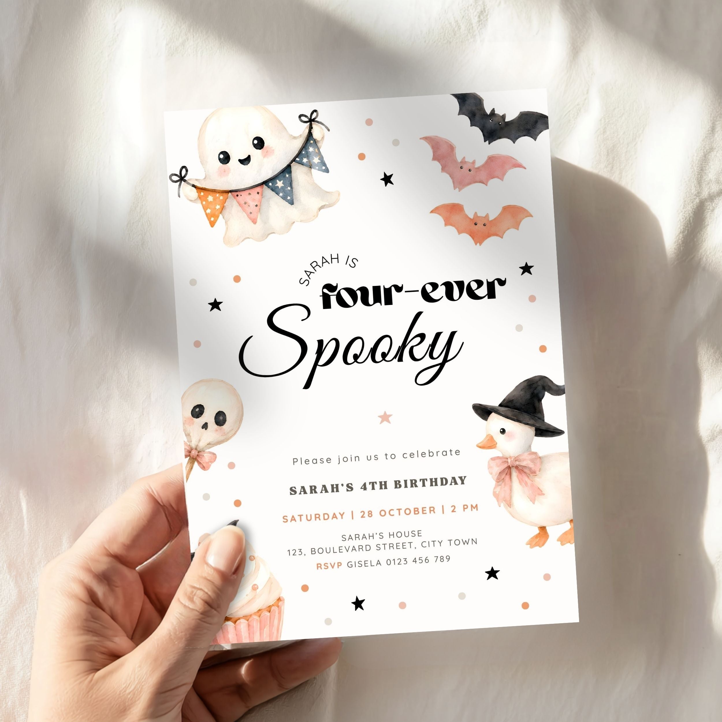 A hand holding a Halloween-themed birthday invitation card. The card features cute illustrations of a ghost, a pumpkin, a witch chick, and bats on a white background with black text reading 'Sarah is four-ever Spooky'.