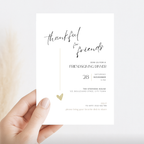 Hand holding a minimal Friendsgiving invitation card with black script and gold details