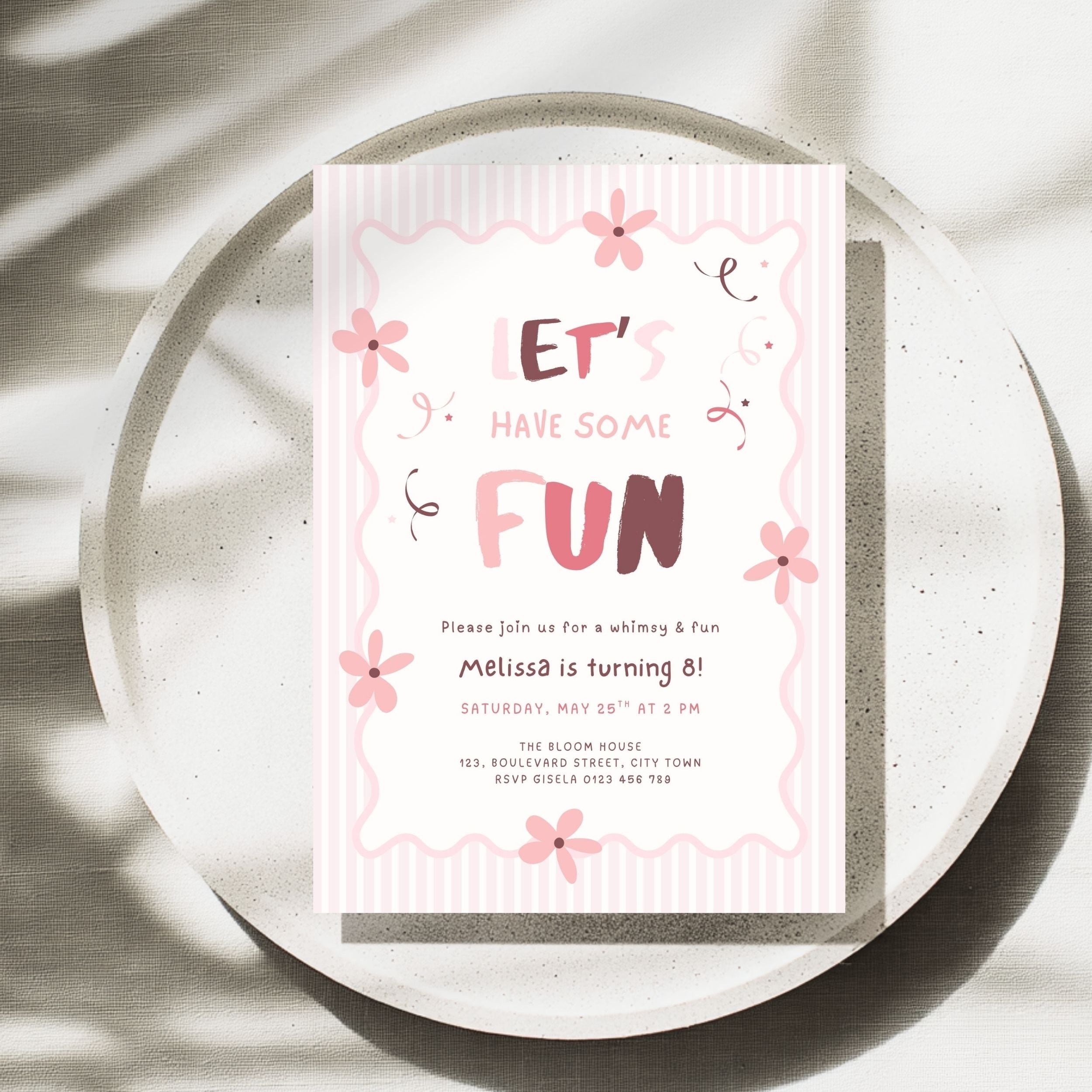 A pink and white birthday invitation card with cute floral doodles and the text 'LET'S HAVE SOME FUN' and 'Melissa is turning 8!', styled on a round speckled tray with soft leaf shadows.