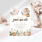 A first boo day invitation card styled in a soft, neutral setting with dried flowers in the background. The card features a white base with illustrations of cute cartoon ghosts, pumpkins, stars, and a circular photo placeholder of a baby.