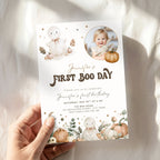 A hand holds a personalized Halloween first birthday invitation card. The card features cute watercolor illustrations of a bunny, pumpkins, and stars, with a circular photo of a young girl and the text 'Jennifer's FIRST BOO DAY'.