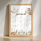 A framed baby first birthday milestone poster with cute illustrations of a baby bunny, pumpkin, stars, and a photo circle, leaning against a wall on a wooden surface.