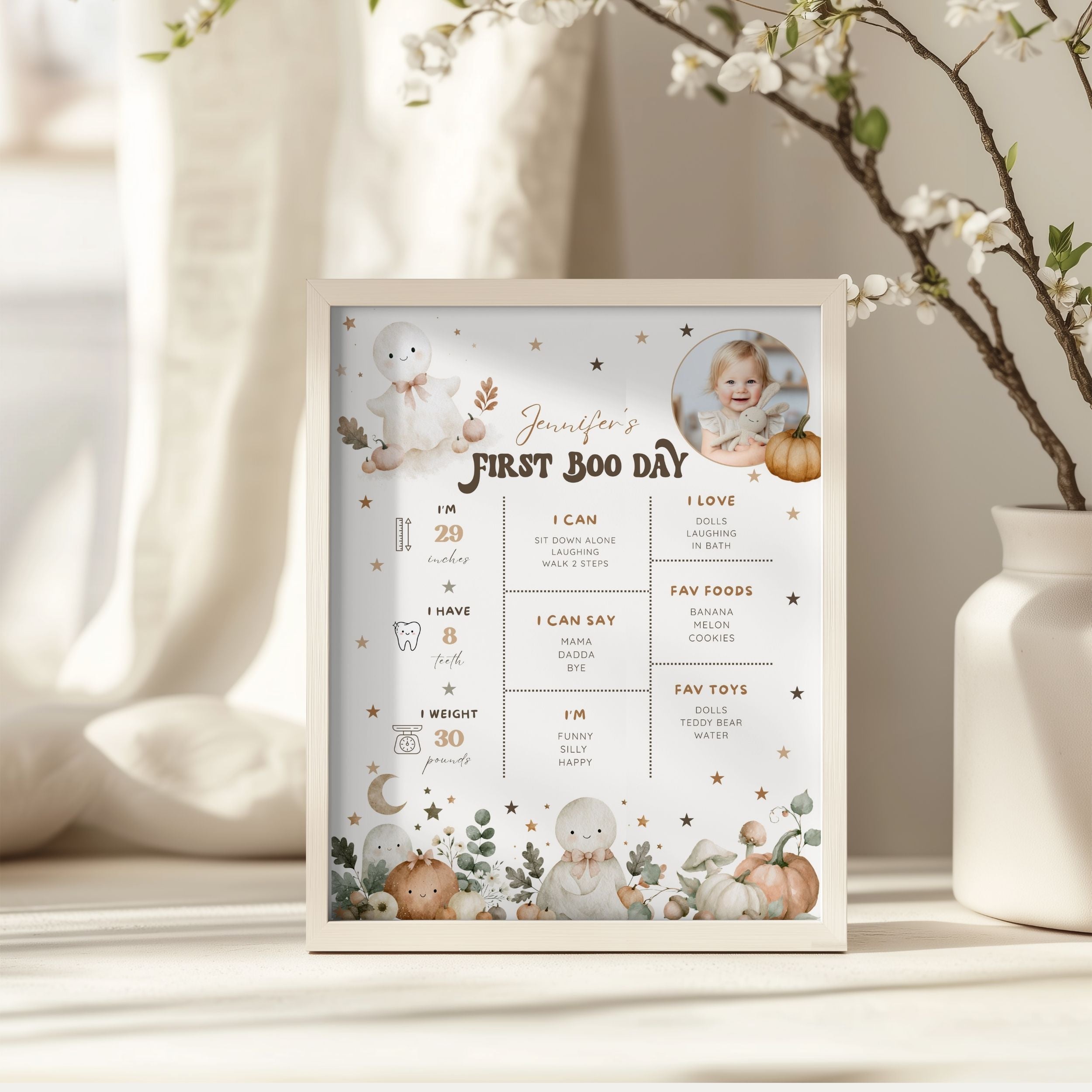 A framed baby first birthday milestone poster displayed on a tabletop. The white frame contains a pastel illustration of a baby, cute animals, stars, and text sections for first birthday achievements and milestones.