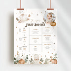 A personalized first boo day milestone poster for a baby, featuring cute illustrations of bears, pumpkins, and fall leaves on a cream background. The poster includes customizable text sections for the baby's name, age, skills, foods, and toys, and is shown hanging from two copper-colored clips against a light gray wall.
